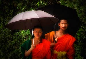 Two Cambodian monks in red robes holding black umbrellas